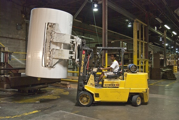 Worker driving forklift carrying large roll of paper