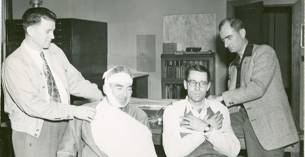 Archival photo of four workers and first aid training