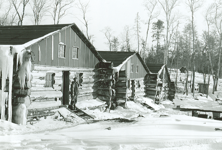 Archive photo of worker standing in cabin doorway of winter logging camp