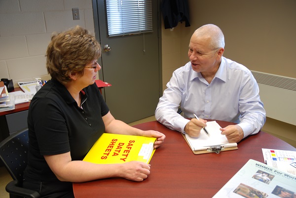 Man and woman sitting at table in workroom reviewing binder