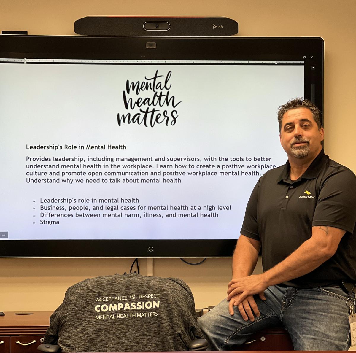 Dennis S sitting in front of large monitor with Mental Health Matters displayed on screen