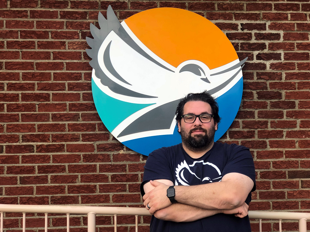 Photo of man standing in front of logo on brick wall